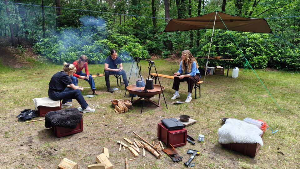 Bushcraft kampplek met tarp, vuur en deelnemers in het bos