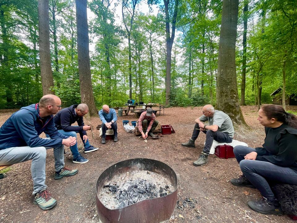 Groep zit in een kring rond het vuur en werkt aan bushcraft skills